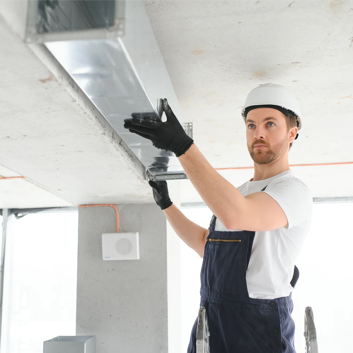 HVAC technician installing metal ductwork overhead